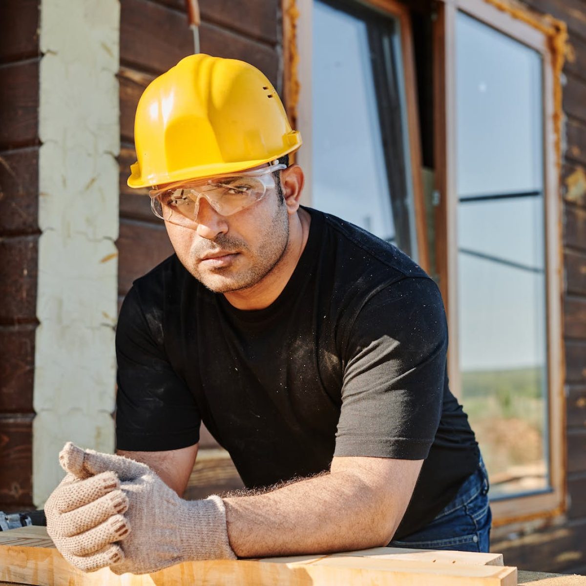 Man in Black Crew Neck T-shirt Wearing Yellow Hard Hat While Standing by the Wooden Table